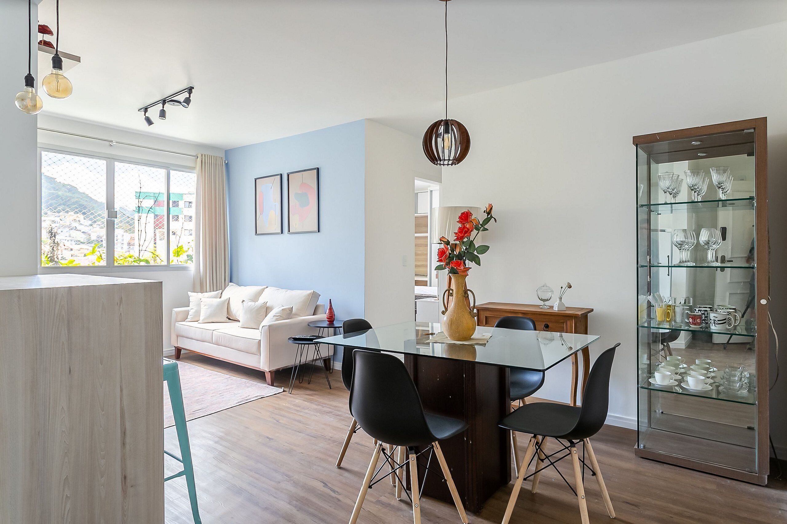 A modern living room with a glass dining table, black chairs, a white sofa, and a glass cabinet with decorative items.