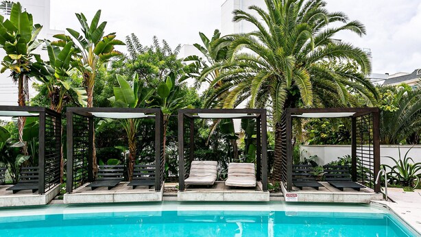 Ein Poolbereich mit Liegestühlen und einer Pergola, umgeben von tropischen Pflanzen.