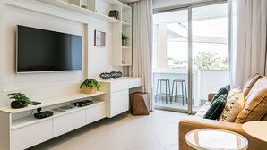 Ein modernes Wohnzimmer mit Flachbildfernseher, weißen Regalen, einem Couchtisch und einer Couch mit Kissen.