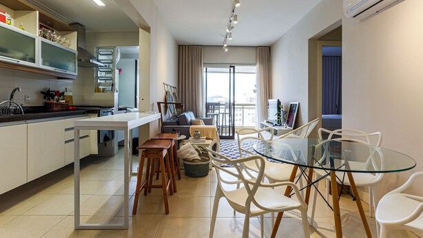 A modern kitchen with white cabinets, a dining area with a glass table and white chairs, and a living area with a sofa and a TV. - 350m Public Market | Walkable #CA10 (Florianópolis)