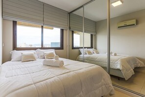 A hotel room with a large bed, a mirror, and a window with blinds.