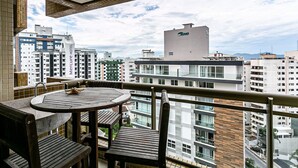 A balcony with a round wooden table and chairs, overlooking a cityscape with high-rise buildings and a clear sky. - 350m Public Market | Walkable #CA10 (Florianópolis)