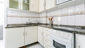 A kitchen with white cabinets, a granite countertop, a stove, and a microwave. - WI-FI 120MB | 120m from Beiramar Shopping #CA31 (Florianópolis)