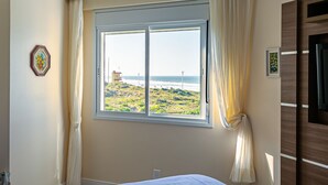 A bedroom with a large window offering a view of the beach and ocean. - SEA VIEW | Balcony with Barbecue #IA09 (Florianópolis)