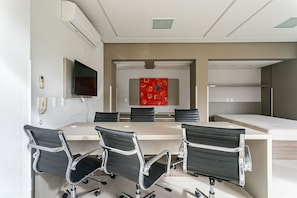 Conference room with a long table and six chairs, featuring a flat-screen TV and artwork.