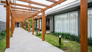 Une allée couverte avec des poutres en bois, un chemin pavé et une zone herbeuse agrémentée de plantes.