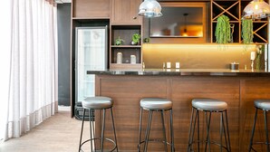Une cuisine moderne avec des meubles en bois, un îlot central doté de tabourets, un éclairage suspendu et une vue sur l’extérieur.