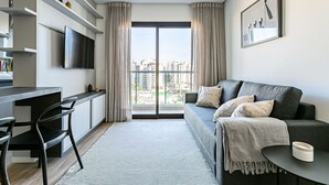 Un salon moderne avec un canapé, un téléviseur fixé au mur et une grande fenêtre avec des rideaux.