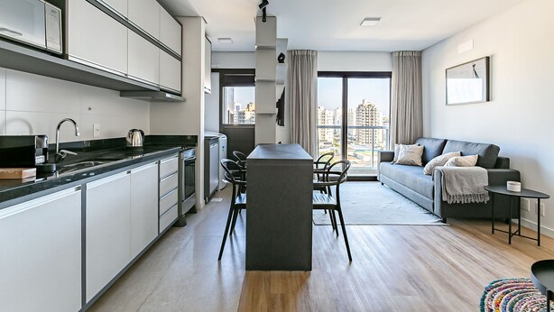 Une cuisine moderne dotée d’un îlot central, d’un coin repas avec des chaises, d’un canapé et offrant une vue sur la ville grâce à de grandes fenêtres.