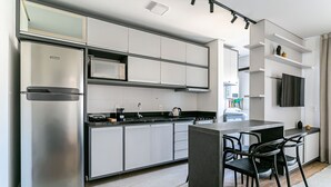 Une cuisine moderne avec un réfrigérateur en acier inoxydable, des armoires blanches, un plan de travail noir et des chaises noires.