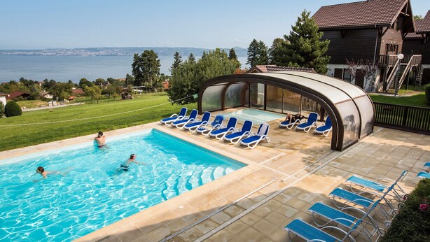 Una piscina con sillas azules, una zona techada y vista al mar.