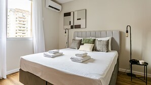 A neatly made bed with folded towels, a grey headboard, and two wall-mounted light fixtures. - WI-FI 350MB | 200m from Beiramar Shopping #CA29 (Florianópolis)