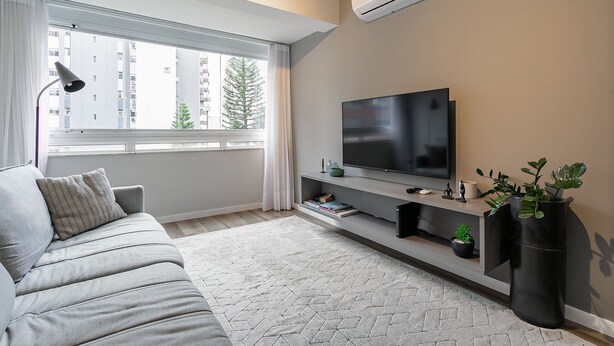 A modern living room with a grey sofa, a flat-screen TV, a large window with curtains, and a potted plant. - WI-FI 350MB | 200m from Beiramar Shopping #CA29 (Florianópolis)