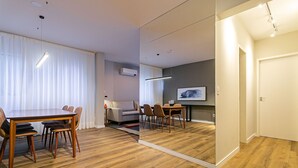 Ein modernes Zimmer mit Holzboden, einem Esstisch mit Stühlen, einer Couch und einem Flachbildfernseher.