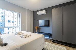 A modern bedroom with a large bed, a TV mounted on the wall, and a wardrobe. - Partial SEA View | 150m from Shopping #CA40 (Florianópolis)