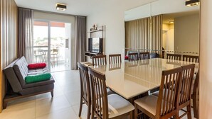 Ein moderner Essbereich mit großem Tisch und Holzstühlen, einer Couch mit Kissen, einem Fernseher und einer Glasschiebetür, die zu einem Außenbereich führt.