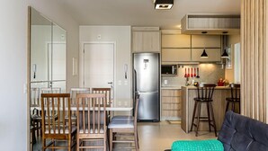 Eine moderne Küche mit Kühlschrank, Mikrowelle und Barhocker. Es gibt einen Essbereich mit Holzkästen und ein Sofa mit einem grünen Kissen.