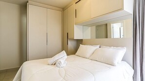 Ein Hotelzimmer mit einem ordentlich bezogenen Bett, einem großen Kleiderschrank und einem Spiegel über dem Bett.