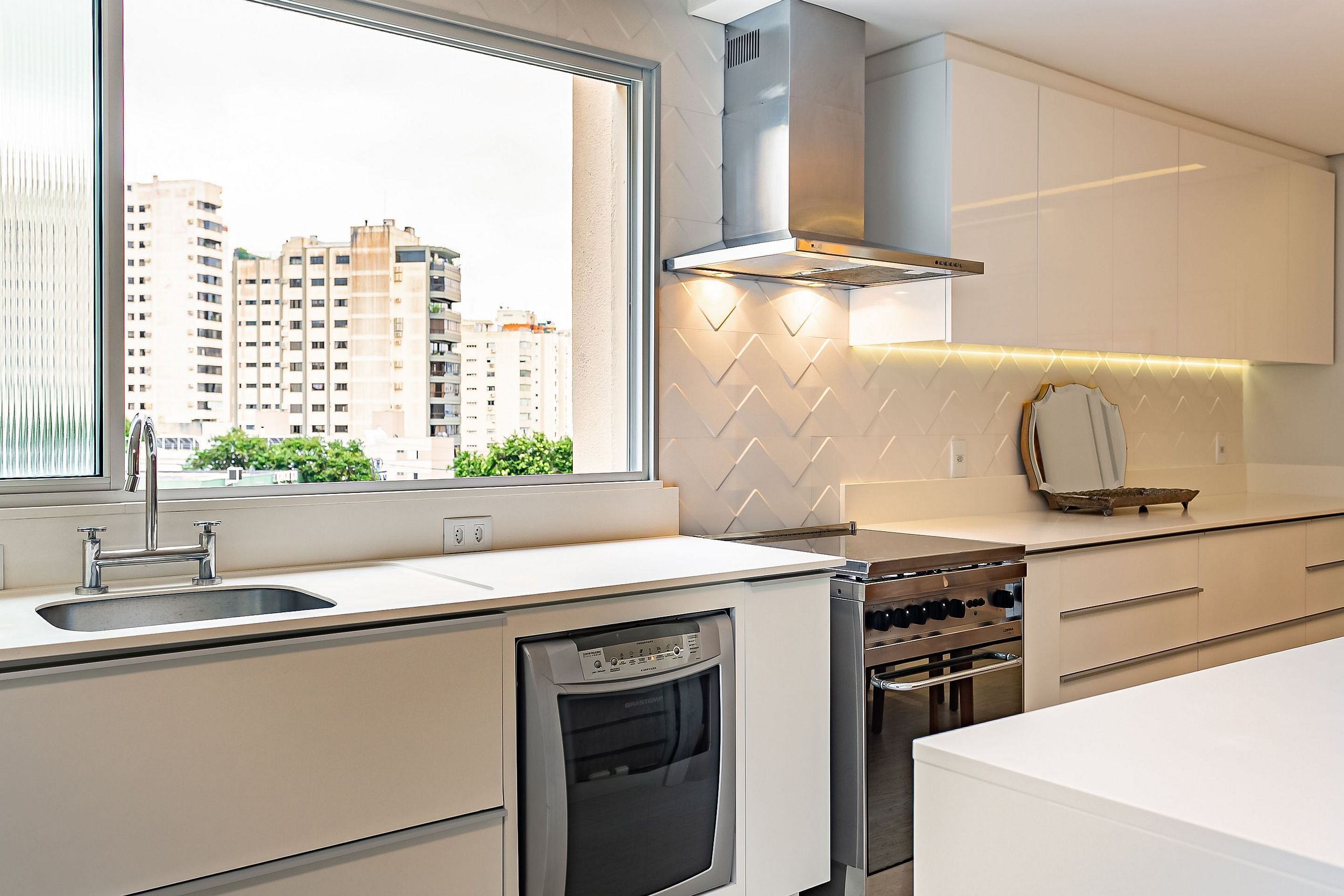 A modern kitchen with a built-in dishwasher, stove, and a window offering a city view.