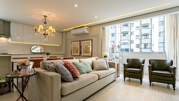 A modern living room with a beige sofa, two armchairs, a chandelier, and a large window with a view of buildings. - WI-FI 240MB | Downtown Florianópolis #CA19 (Florianópolis)