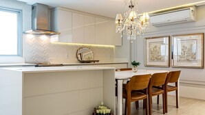 A modern kitchen with a central island, white cabinetry, a chandelier, and framed artwork on the wall. - WI-FI 240MB | Downtown Florianópolis #CA19 (Florianópolis)