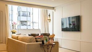 A living room with a sofa, a small table with a lamp, a TV mounted on the wall, and a window with curtains. - WI-FI 240MB | Downtown Florianópolis #CA19 (Florianópolis)