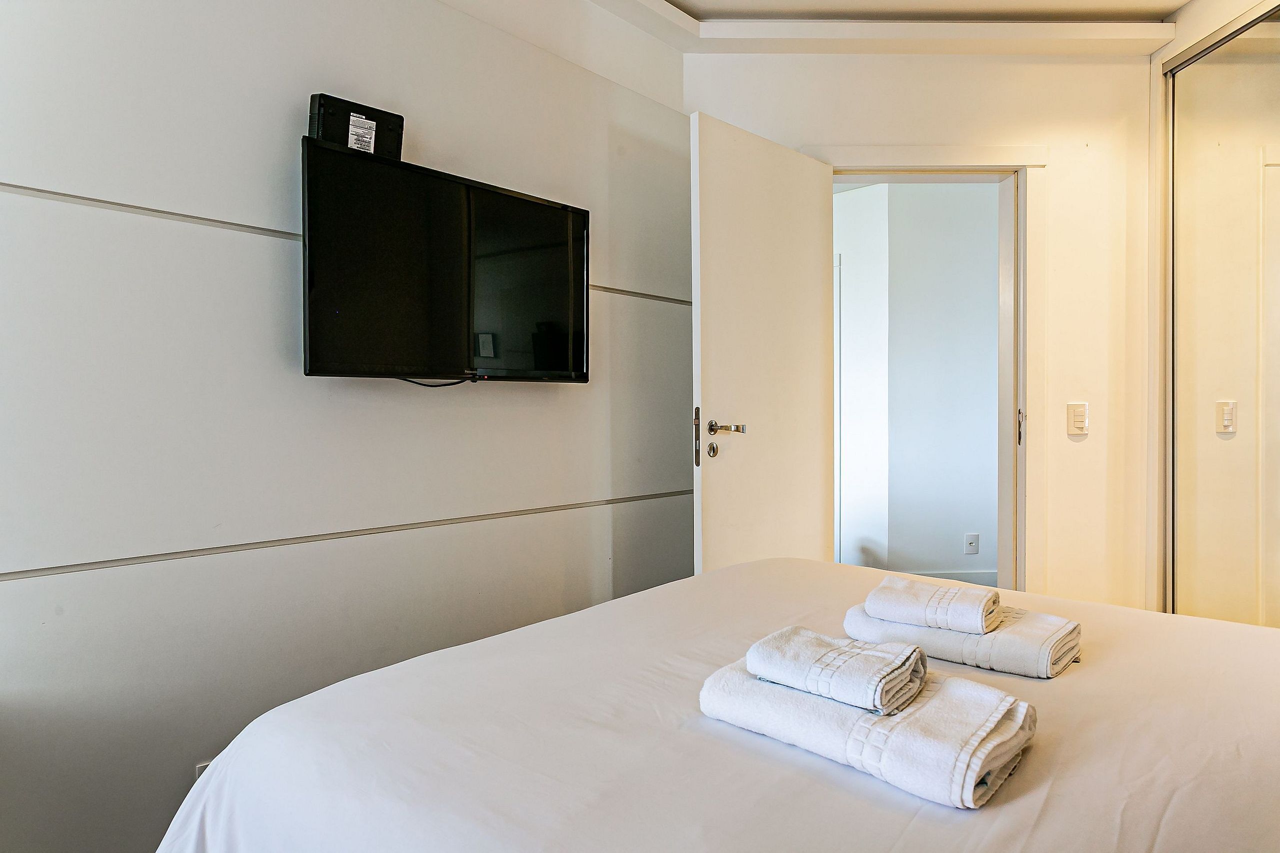Une chambre d’hôtel avec un lit, un téléviseur à écran plat fixé au mur et une porte donnant sur une autre pièce.