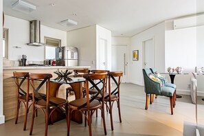 A modern kitchen with a dining area, featuring a central island, wooden chairs, and a teal armchair.