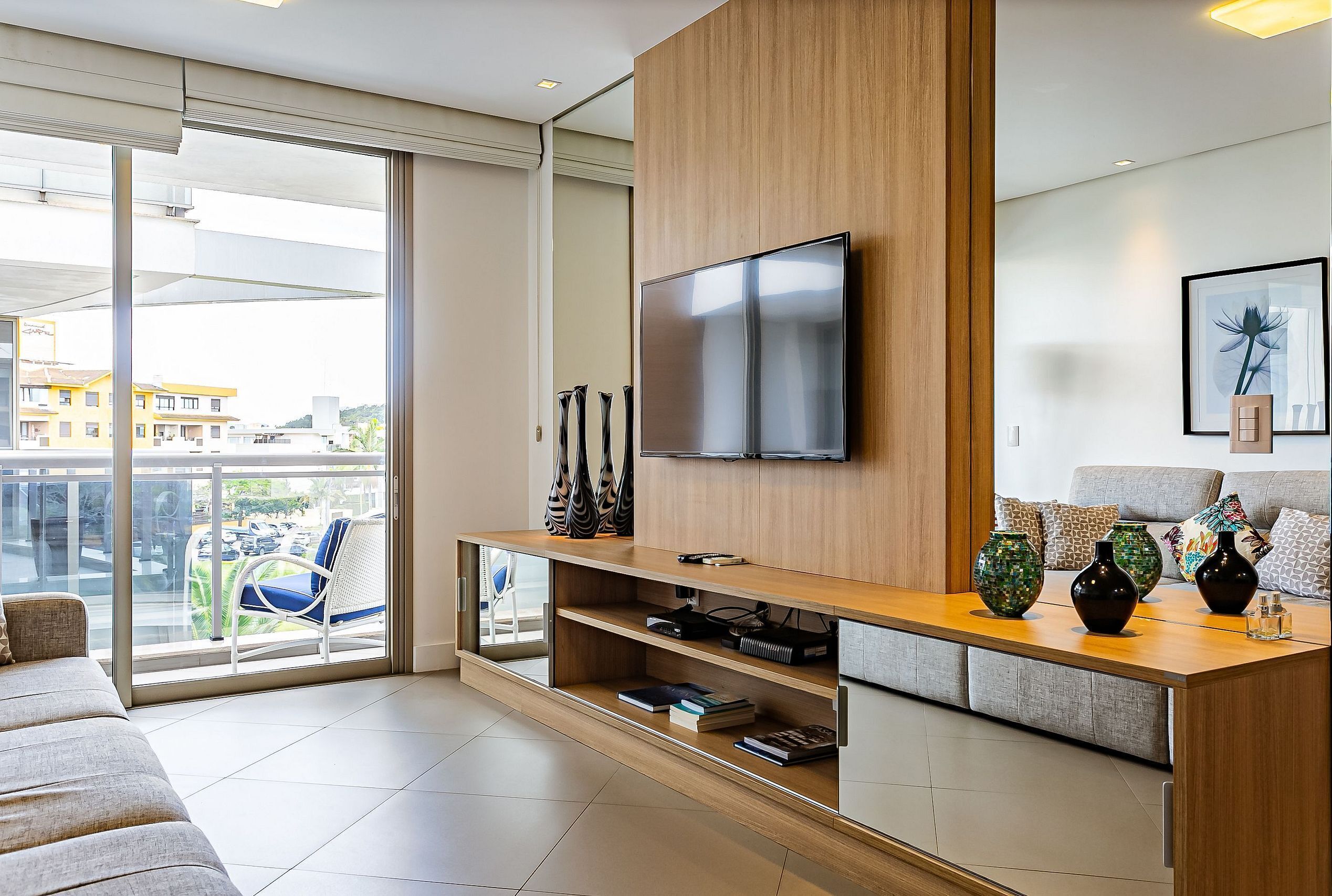 Een moderne woonkamer met een grote televisie, houten lambrisering, een balkon met uitzicht en een bank.