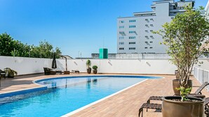 A rooftop swimming pool with lounge chairs and potted plants.