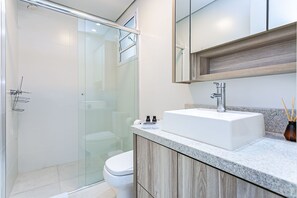 A modern bathroom with a glass shower enclosure, a white sink, and a wooden vanity. - WI-FI 100mb | Pool | Partial sea view #CA32 (Florianópolis)