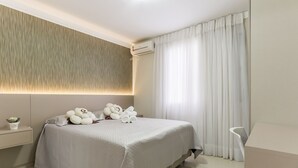 Quarto moderno com uma cama grande, uma mesa de cabeceira com abajur e ar-condicionado fixado na parede.