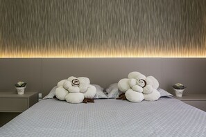 Un lit bien fait, recouvert d’une courtepointe blanche, agrémenté de deux grands coussins décoratifs, et un mur orné d’une bande lumineuse verticale.