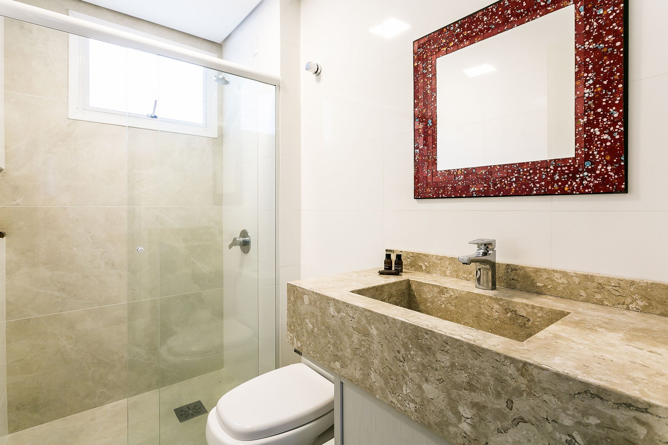 A bathroom with a glass shower enclosure, a white toilet, and a sink with a marble countertop.