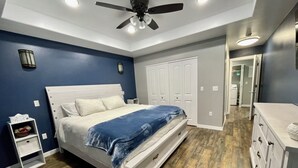 Quarto com cama, penteadeira, mesa de cabeceira, ventoinha no teto e guarda-roupa.