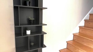 A black wall-mounted shelf with multiple compartments, a wooden staircase, and a white wall. - Close to Old Town Alexandria And All Things DC (Alexandria)