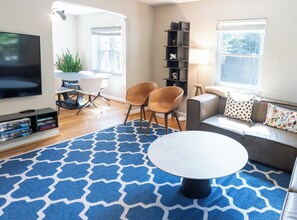 A modern living room with a television, two chairs, a sofa, a coffee table, and a bookshelf. - 3BR Del Ray House - Walk to Metro & Old Town (Alexandria)