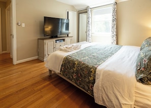Un dormitorio con cama, televisor, cómoda y ventana con cortinas.