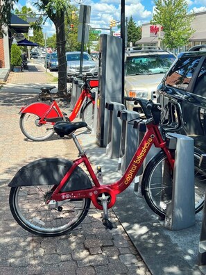 A red bicycle parked at a bike-sharing station with a city street in the background.