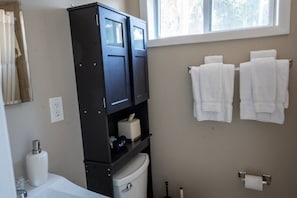 A bathroom with a dark cabinet, a toilet, a sink, and a window.
