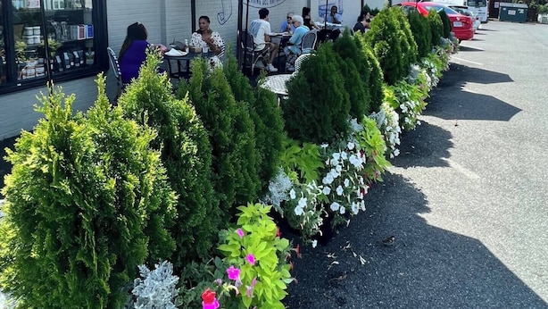 An outdoor seating area with tables and umbrellas, surrounded by greenery and a building with a bakery sign. - Close to Old Town Alexandria And All Things DC (Alexandria)