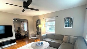 A modern living room with a grey sofa, a round coffee table, a flat-screen TV, and a ceiling fan. - Close to Old Town Alexandria And All Things DC (Alexandria)
