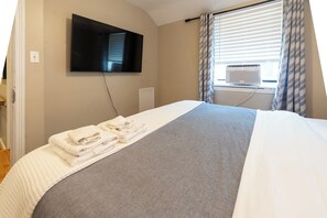 Et hotelværelse med en seng, et fladskærms-TV ophængt på væggen og et vindue med persienner.