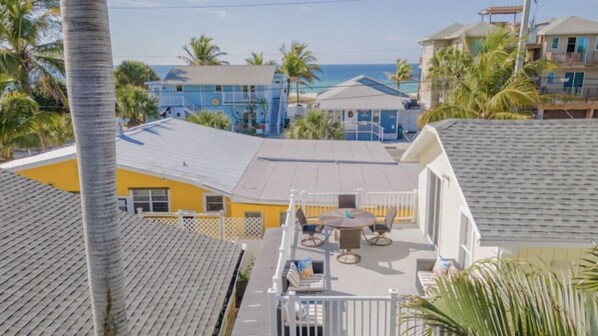 Zona residencial con balcón que incluye una mesa y sillas, rodeada de palmeras y edificios con vistas al océano.