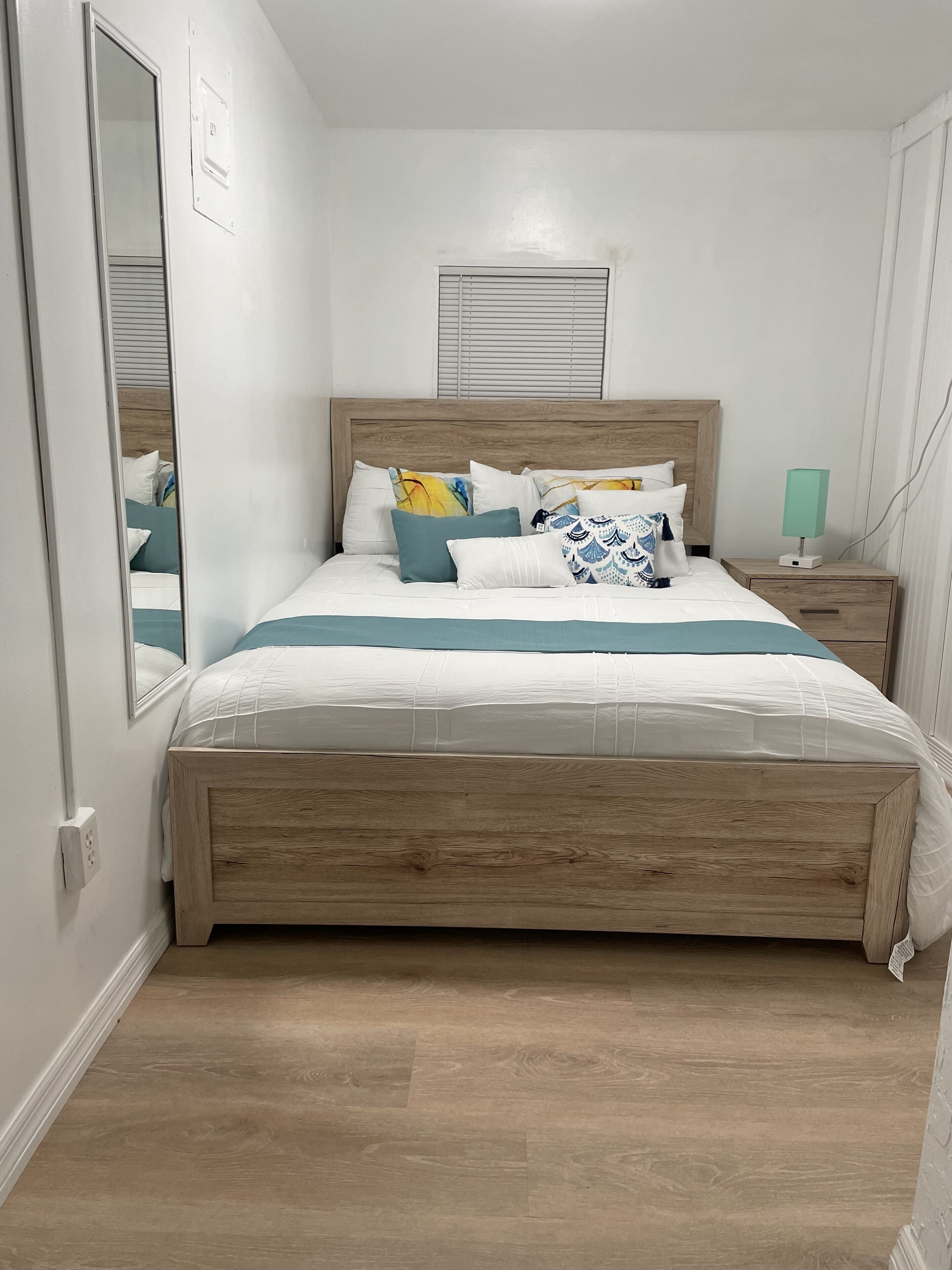 A bedroom with a wooden bed, white bedding, and a nightstand with a lamp.