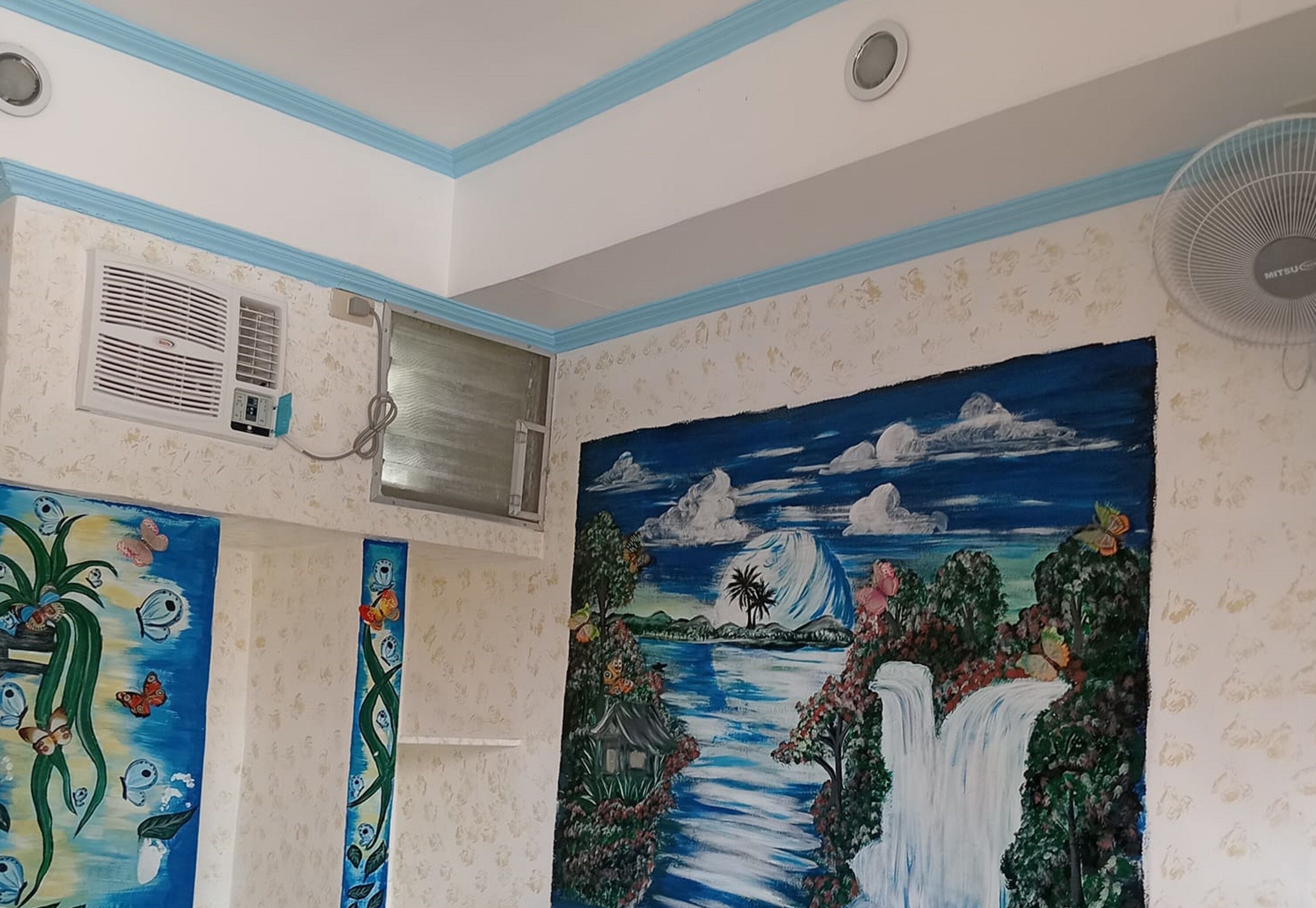 Habitación con un mural de una cascada, un equipo de aire acondicionado y un ventilador de pared.