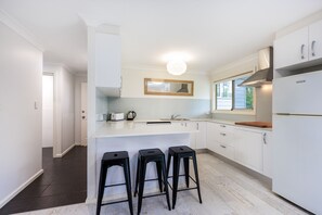 A modern kitchen with white cabinetry, a central island with stools, a built-in oven, and a window providing natural light.