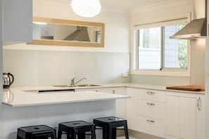 A modern kitchen with a large island, a window, and a pendant light. - Anais Hat Head 5 Bedroom House 10 Guests (Hat Head)