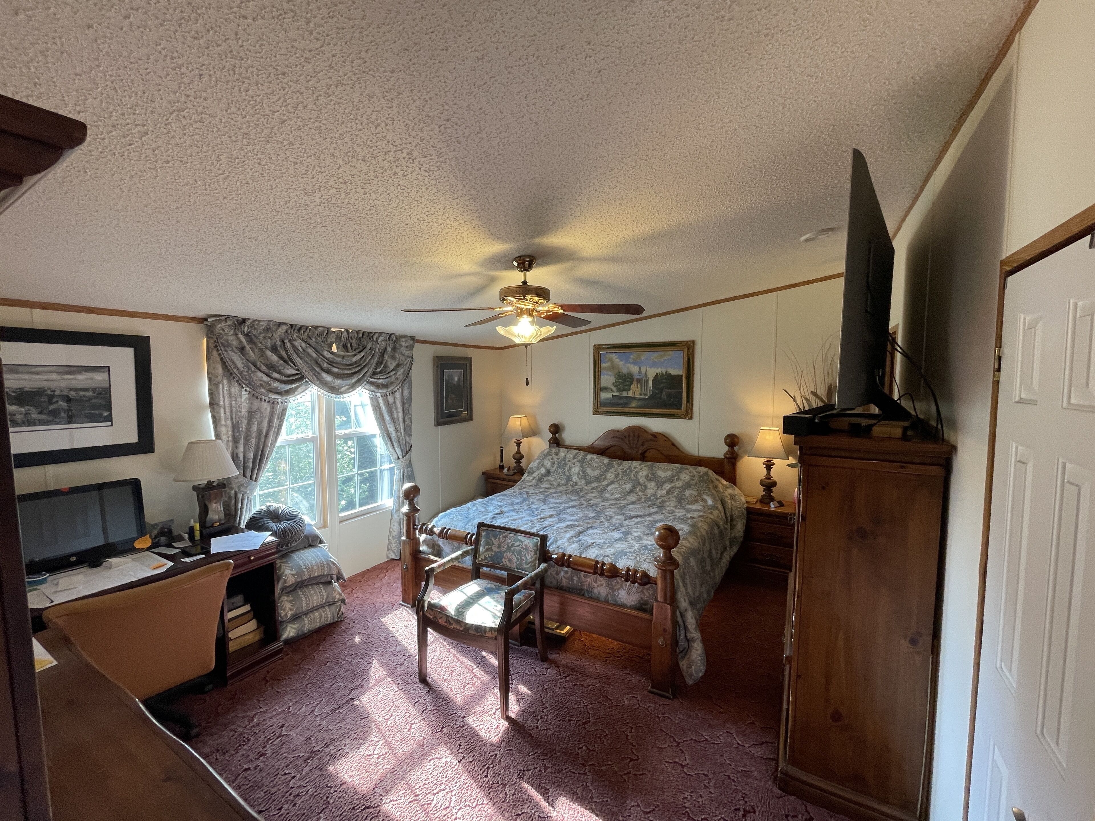 Une chambre à coucher comprenant un lit, un bureau, une chaise, un téléviseur et un ventilateur de plafond.