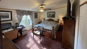 Une chambre à coucher comprenant un lit, un bureau, une chaise, un téléviseur et un ventilateur de plafond.